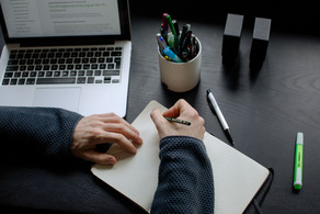 A student working at a table with a laptop, pencils and a notebook.