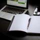 Turned on laptop, smartphone and notebook with pen lying on a table.